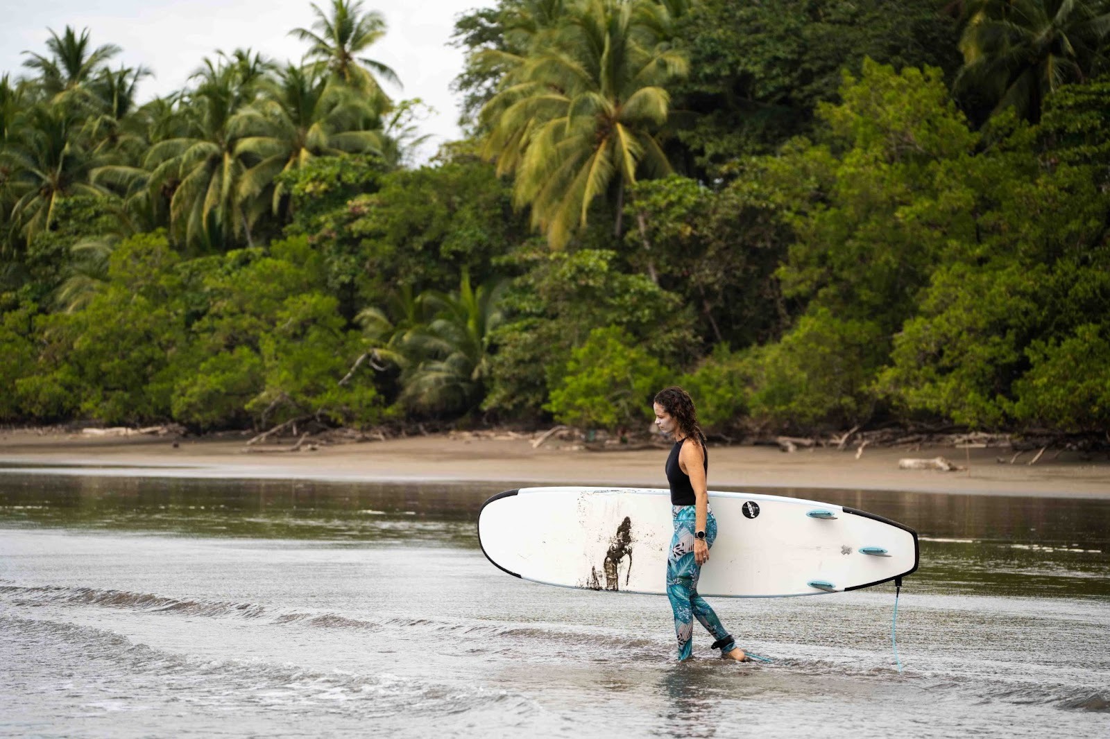 A surfer walking through the jungle path toward the beach in Costa Rica, carrying a surfboard and embracing surfing for personal growth.
